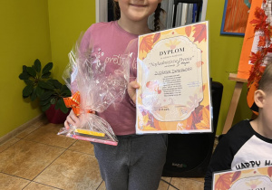 Dziewczynka trzyma w ręku dyplom oraz nagrodę